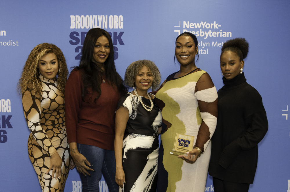 Five women stand together in front of a blue Brooklyn.org SPARK 2026 event backdrop; one woman holds an award plaque.