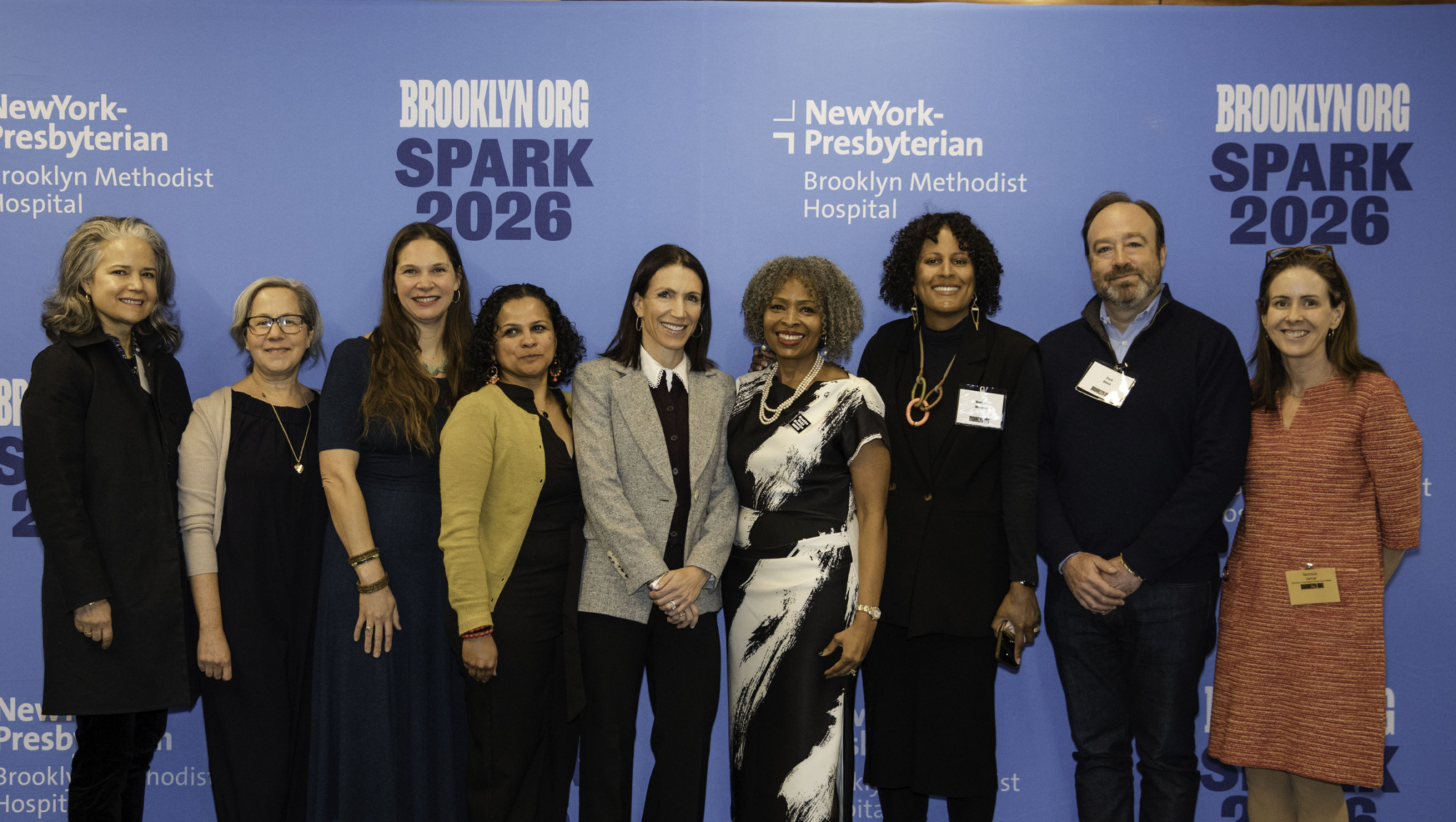 Nine people stand in a row, posing for a group photo in front of a blue backdrop with "NewYork-Presbyterian Brooklyn Methodist Hospital SPARK 2026" printed on it.