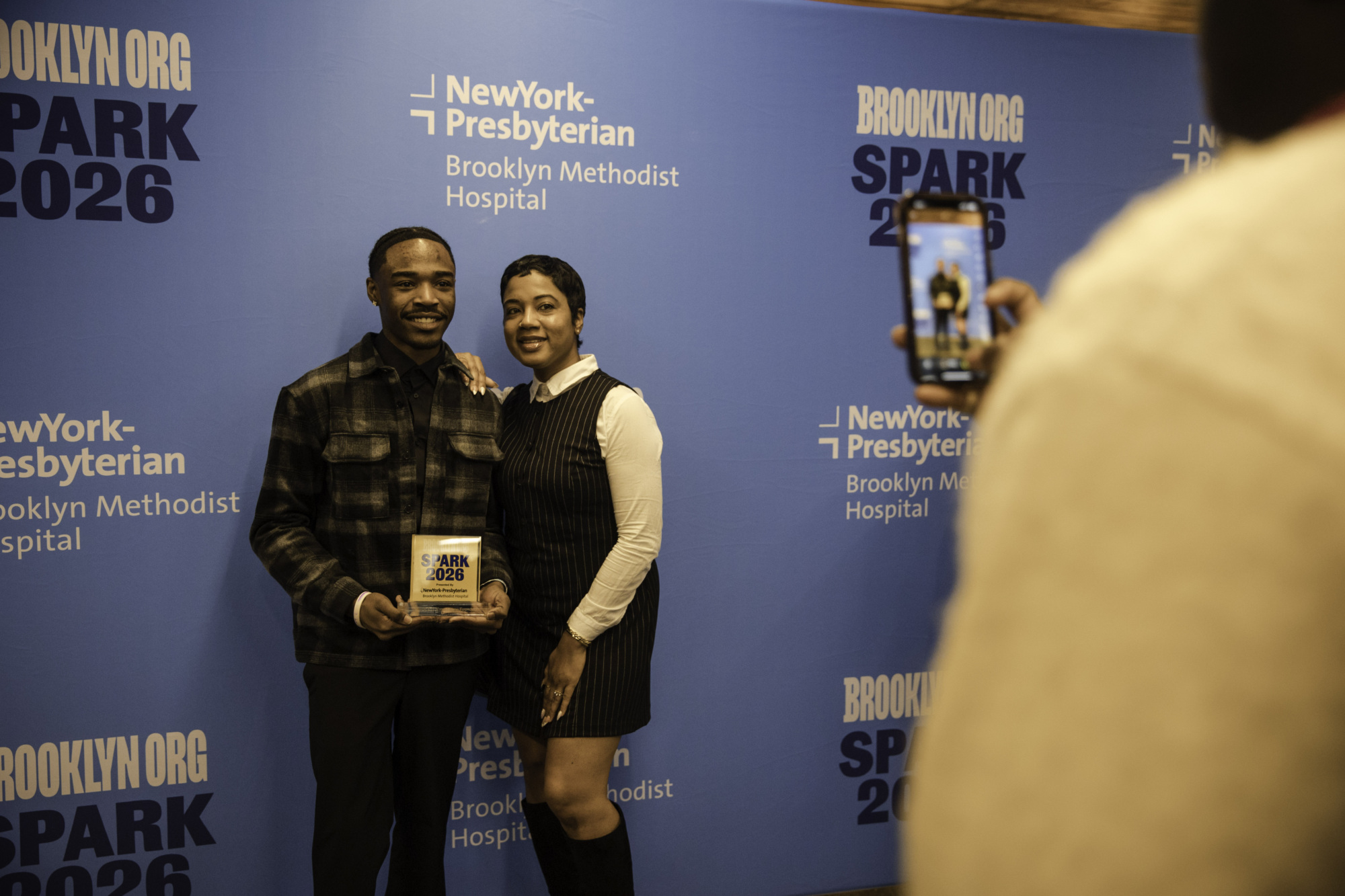 Two people pose for a photo, holding an award, in front of a blue backdrop with "Brooklyn.org SPARK 2026" and "NewYork-Presbyterian Brooklyn Methodist Hospital" logos.