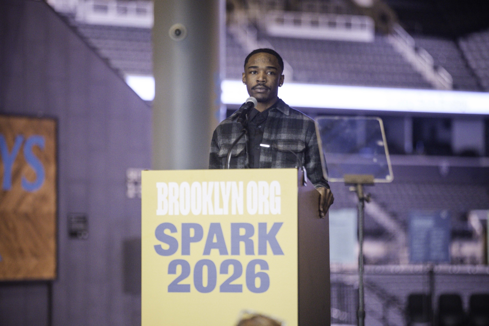 A person stands at a podium labeled "BROOKLYN.ORG SPARK 2026," speaking into a microphone in an indoor venue.