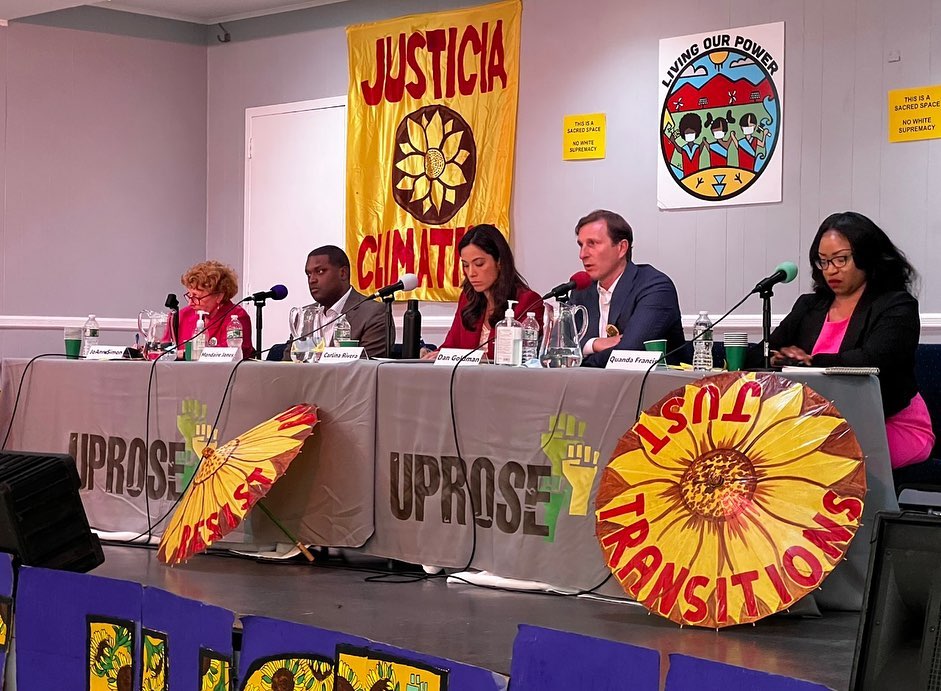 Five panelists sit at a table with microphones during a discussion event. Behind them are banners reading "JUSTICIA CLIMATICA" and "JUST TRANSITIONS.