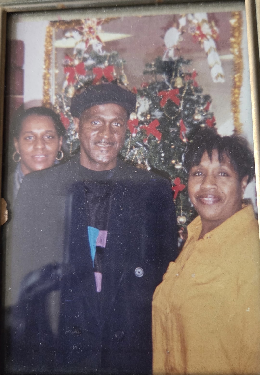 Three adults pose and smile in front of a decorated Christmas tree with red bows and gold garland.