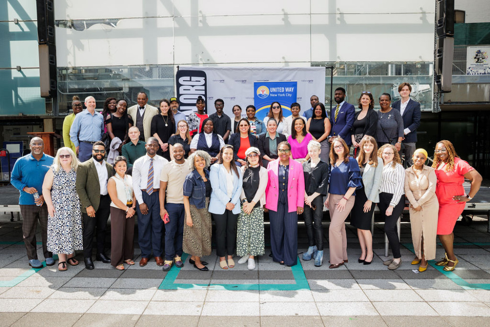 A large group of professionally dressed people pose together outdoors in front of a United Way banner.