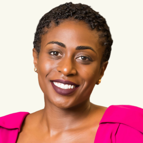 Smiling woman with short curly hair, wearing a bright pink top and gold stud earrings, against a plain light background.
