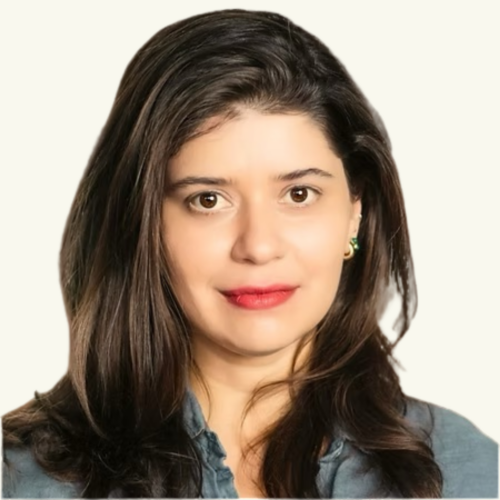Woman with long dark hair wearing a blue shirt, facing forward with a neutral expression and a plain light background.
