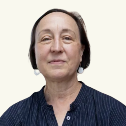 A middle-aged woman with short brown hair, wearing white round earrings and a dark pinstriped blouse, looks at the camera with a neutral expression.
