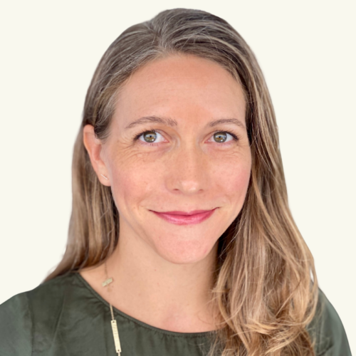 Woman with light brown hair and hazel eyes, wearing a green top and necklace, smiling slightly while facing the camera against a plain light background.