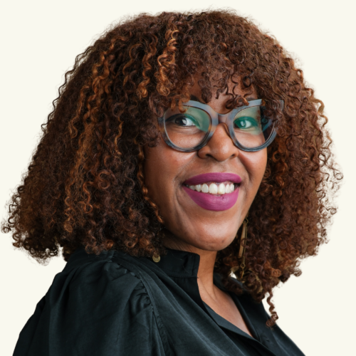 Woman with curly brown hair, glasses, and a black top smiling at the camera against a light background.