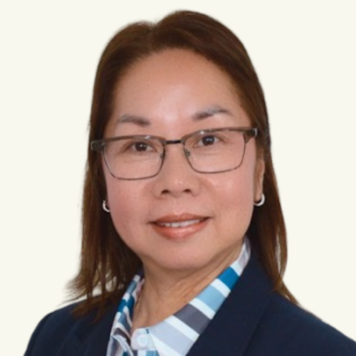 A woman with straight brown hair, glasses, and a navy blazer over a striped shirt, facing forward and smiling slightly against a plain light background.