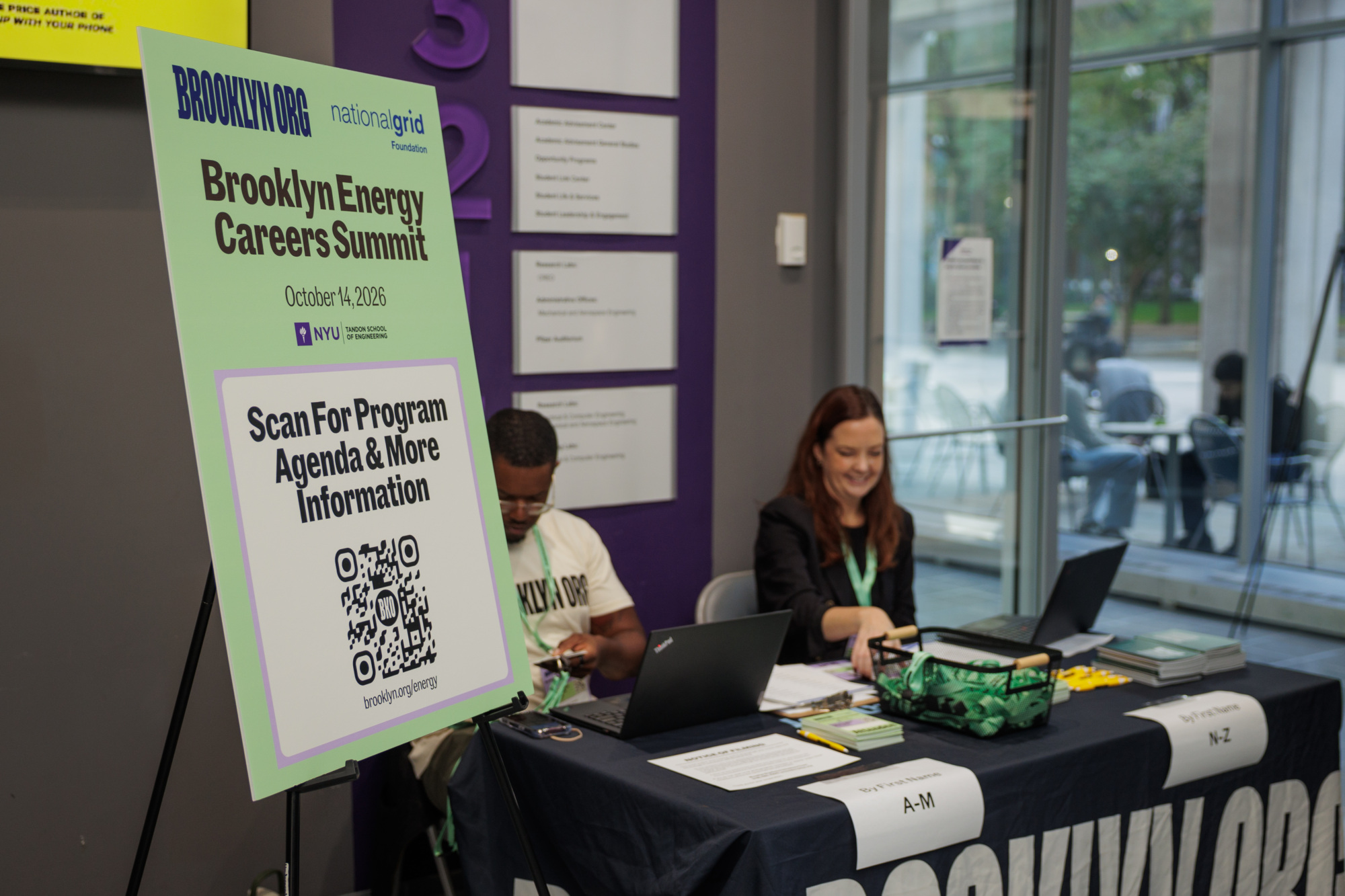 A sign for the Brooklyn Energy Careers Summit on October 14, 2026, with a QR code for the agenda, next to a registration table with two staff members.