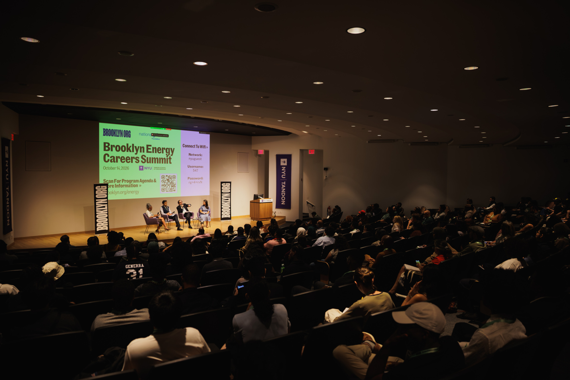 A panel of four people on a stage at the Brooklyn Energy Careers Summit, addressing an audience in a lecture hall.