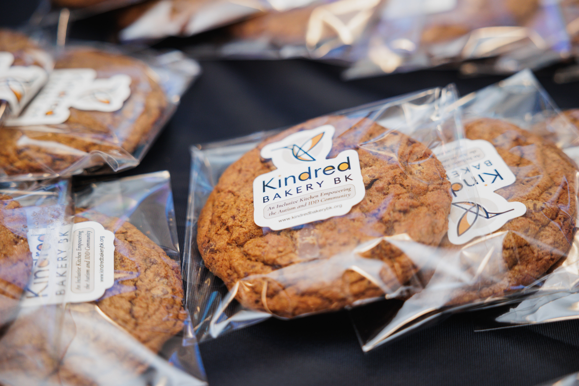 Several chocolate chip cookies individually wrapped in clear plastic, each with a Kindred Bakery BK label.