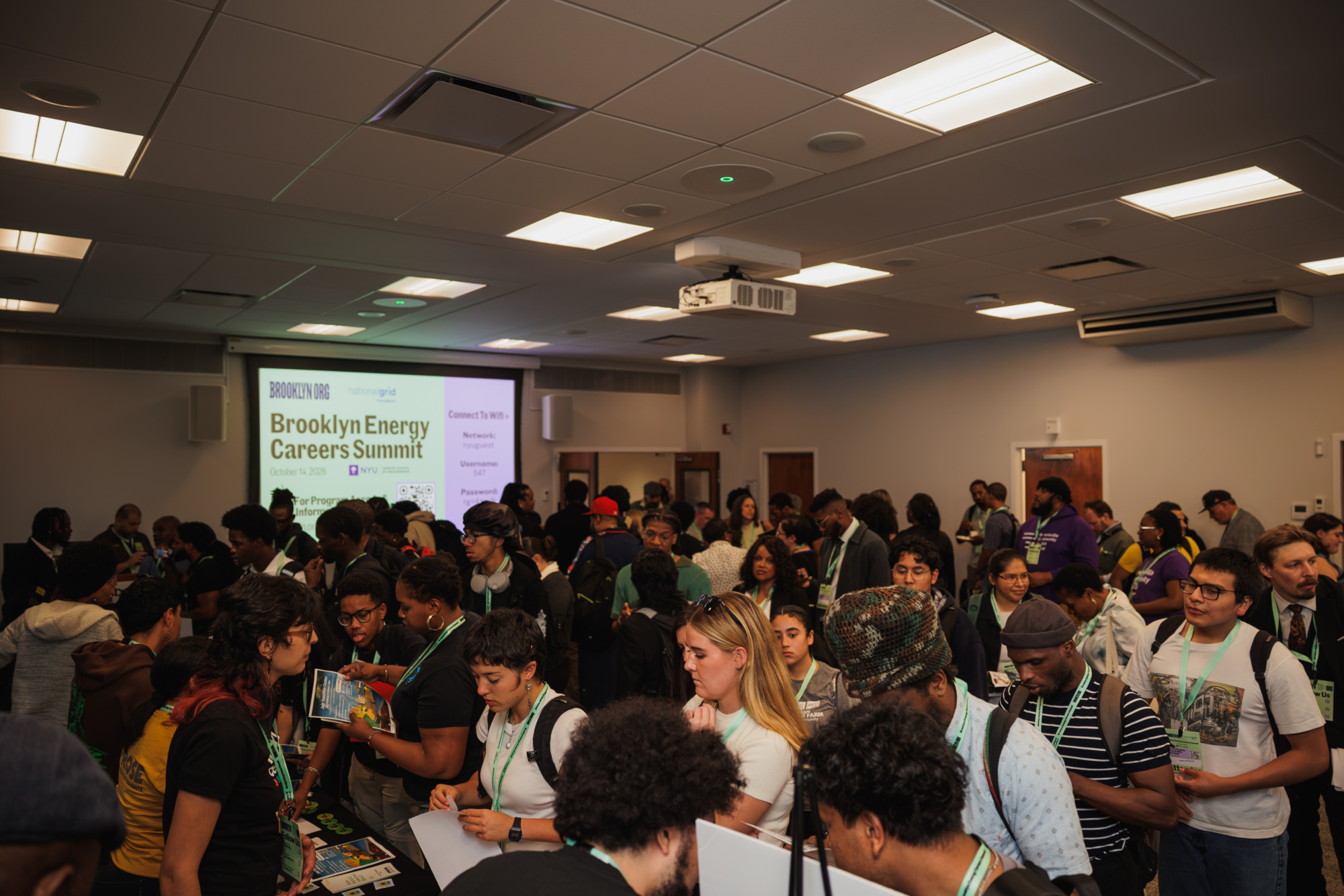 People gathered at the Brooklyn Energy Careers Summit, standing near tables with information brochures.