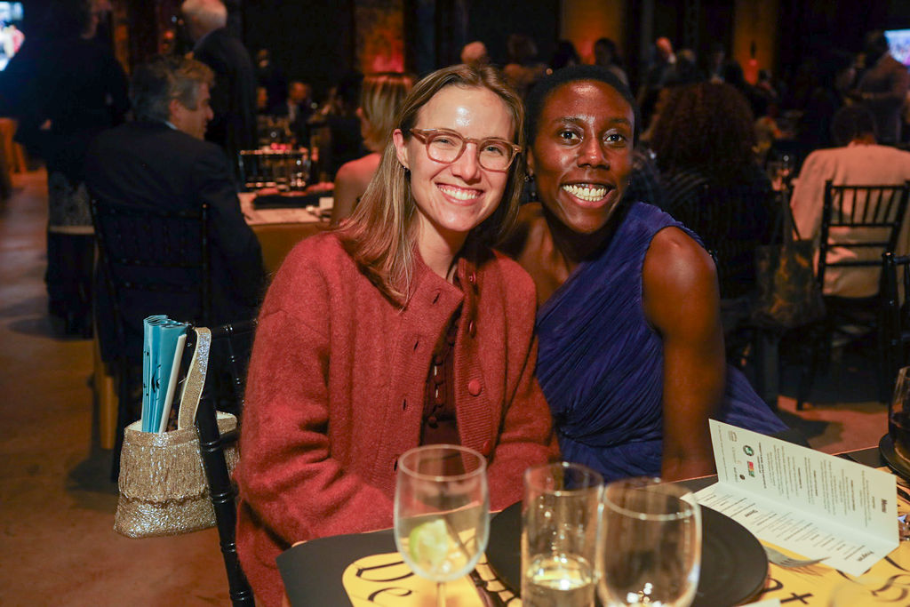 Two women smiling and posing for a photo at an event table.