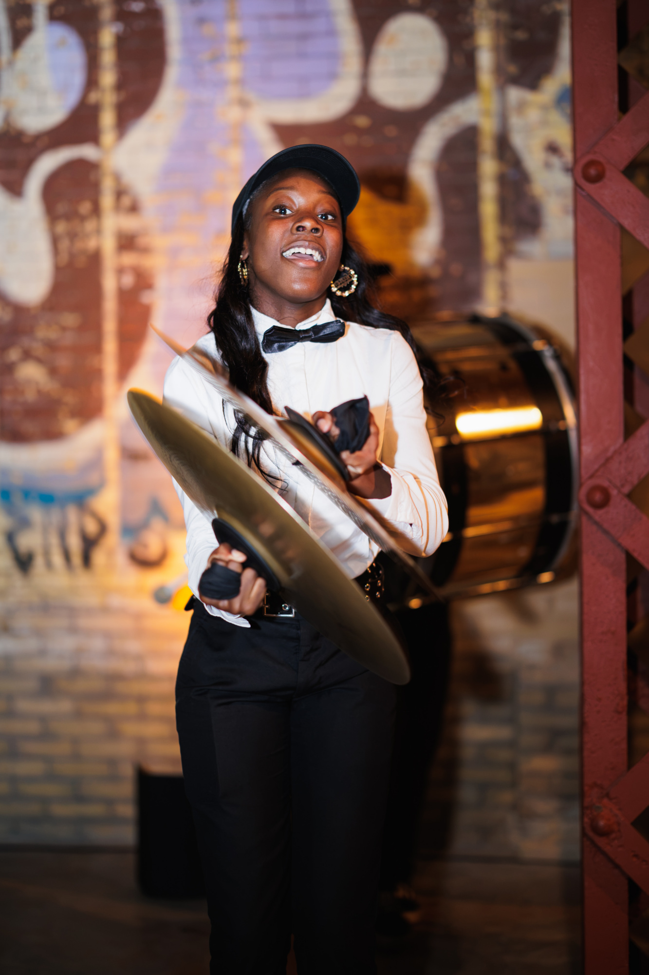 A drummer in a white shirt and bowtie clashing cymbals together.