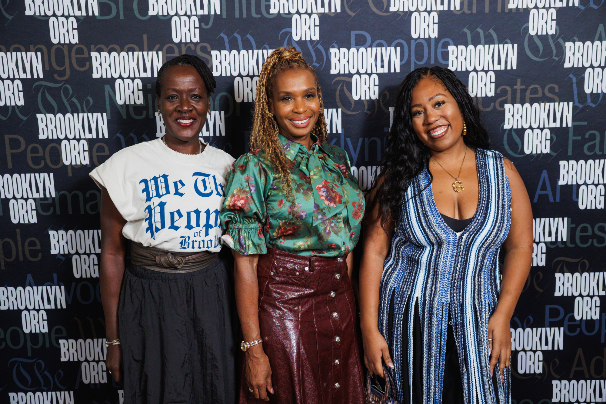 Three women posing in front of a Brooklyn Org step and repeat backdrop.