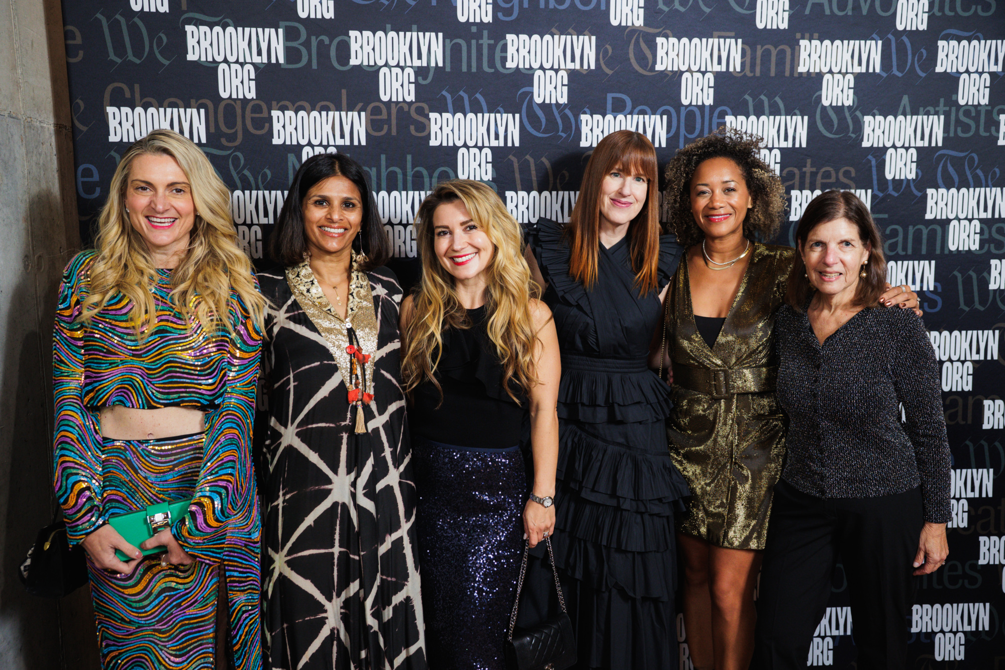 Six women pose for a photo in front of a branded “Brooklyn Org” backdrop.