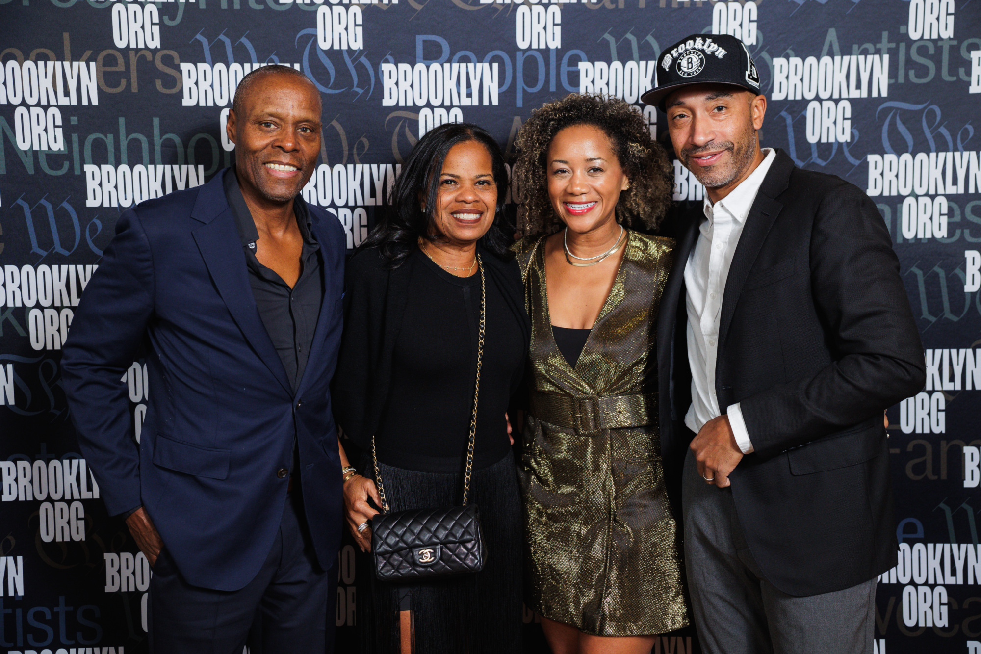 Four people posing for a photo in front of a Brooklyn Org step-and-repeat backdrop.