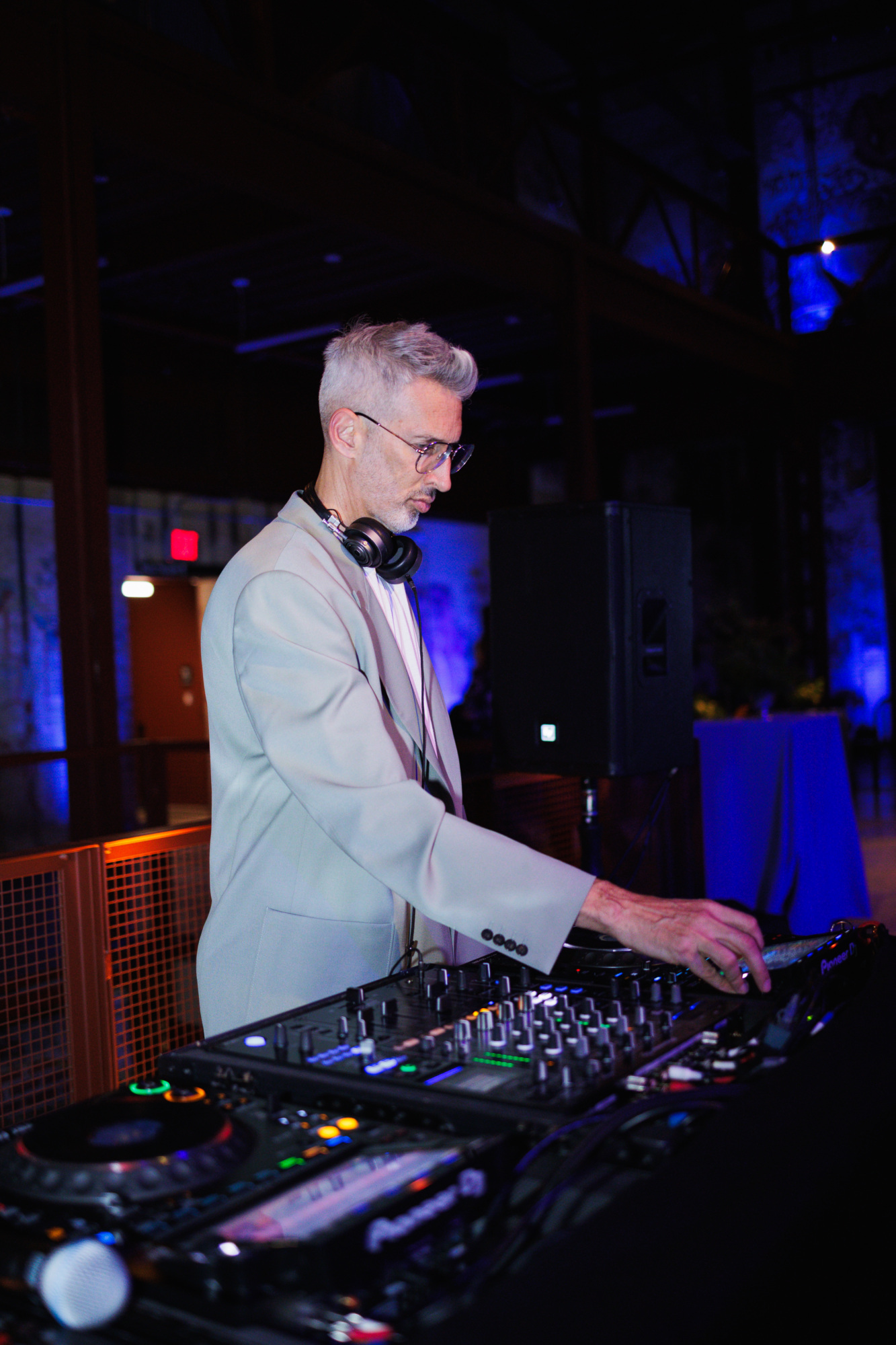A man in a suit and glasses mixing music on a DJ console.