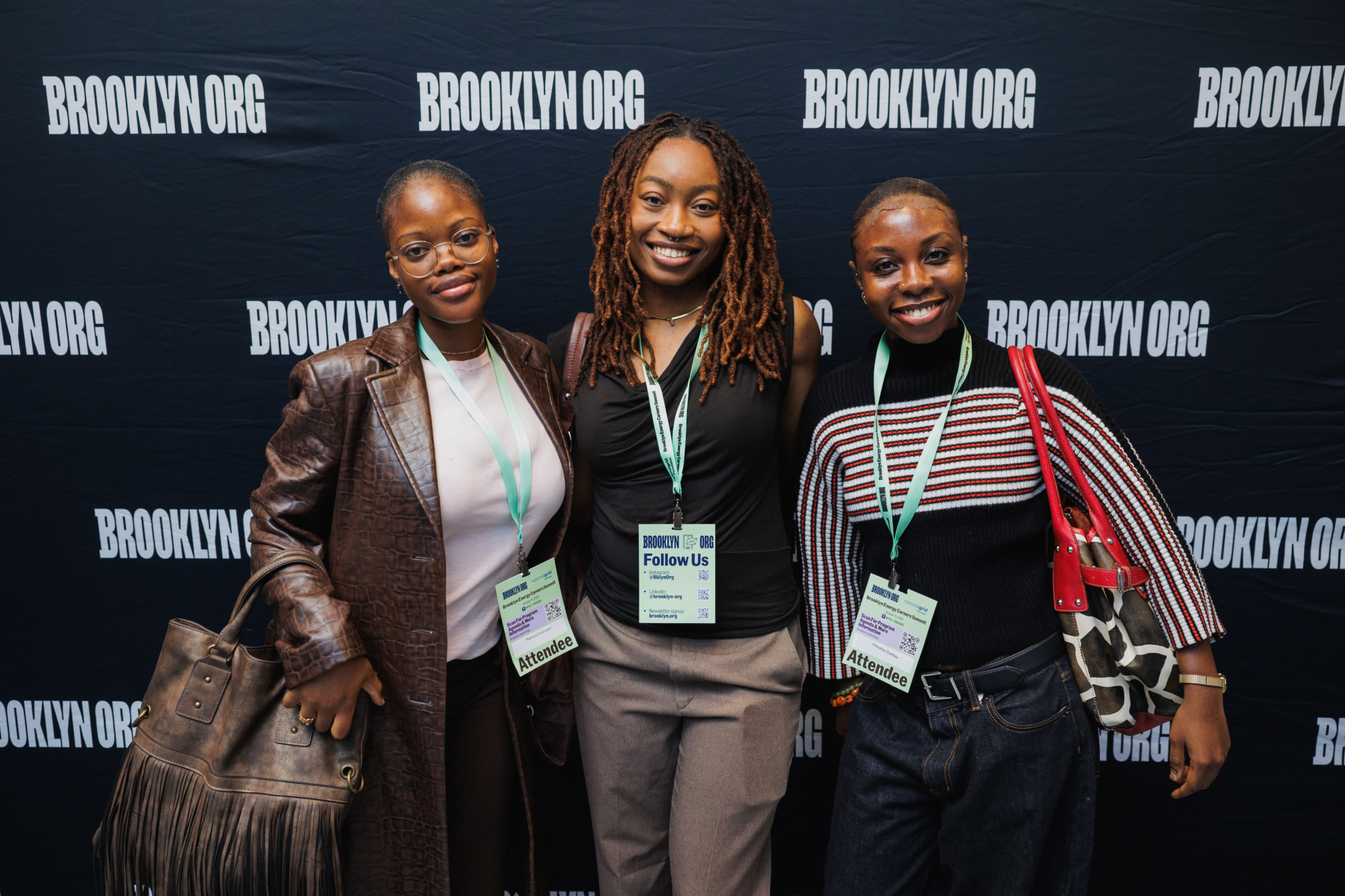Three women posing for a photo in front of a backdrop with the “BROOKLYN ORG” logo, each wearing an event attendee lanyard.