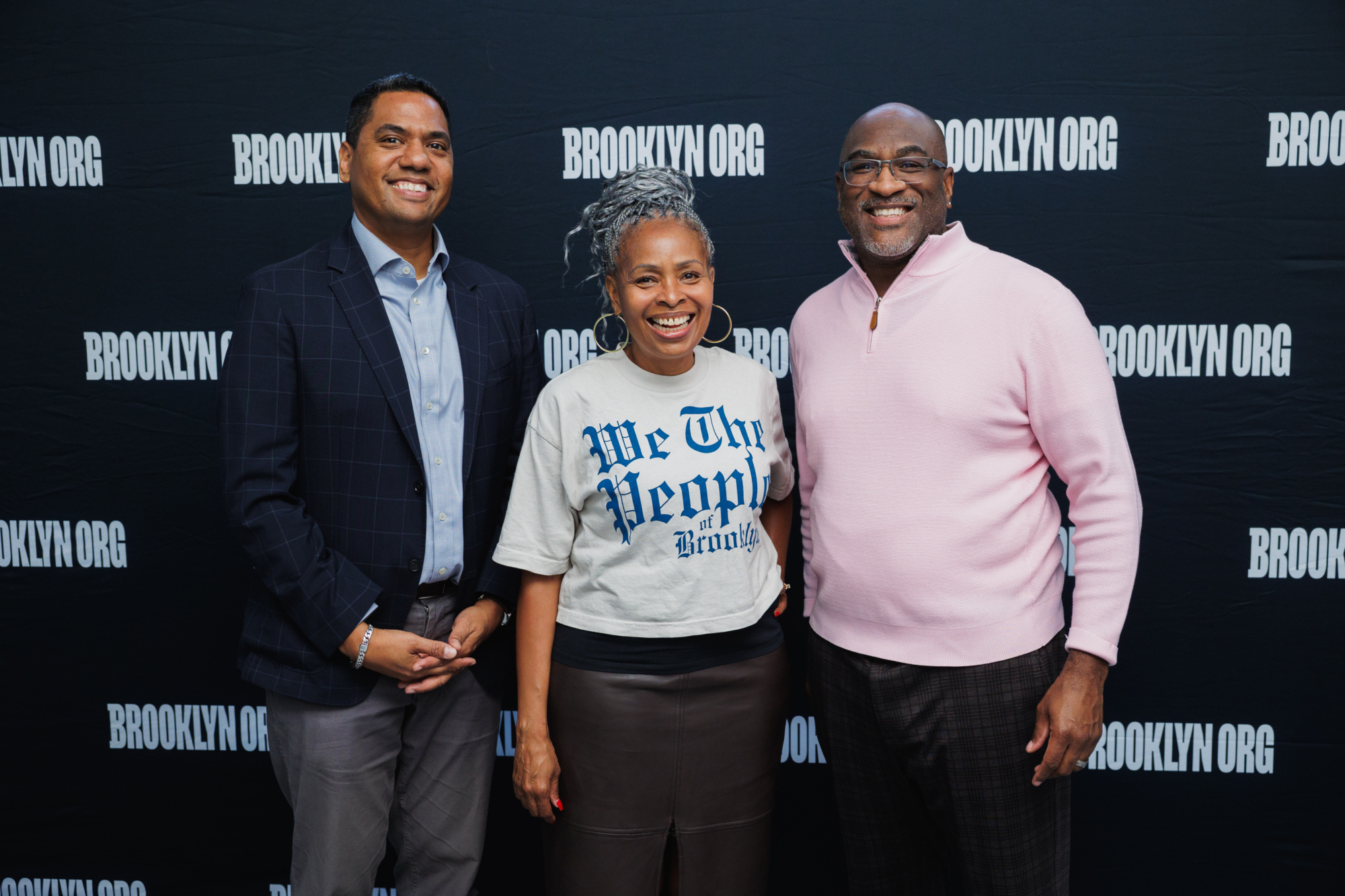 Three people standing in front of a backdrop featuring the Brooklyn.org logo.