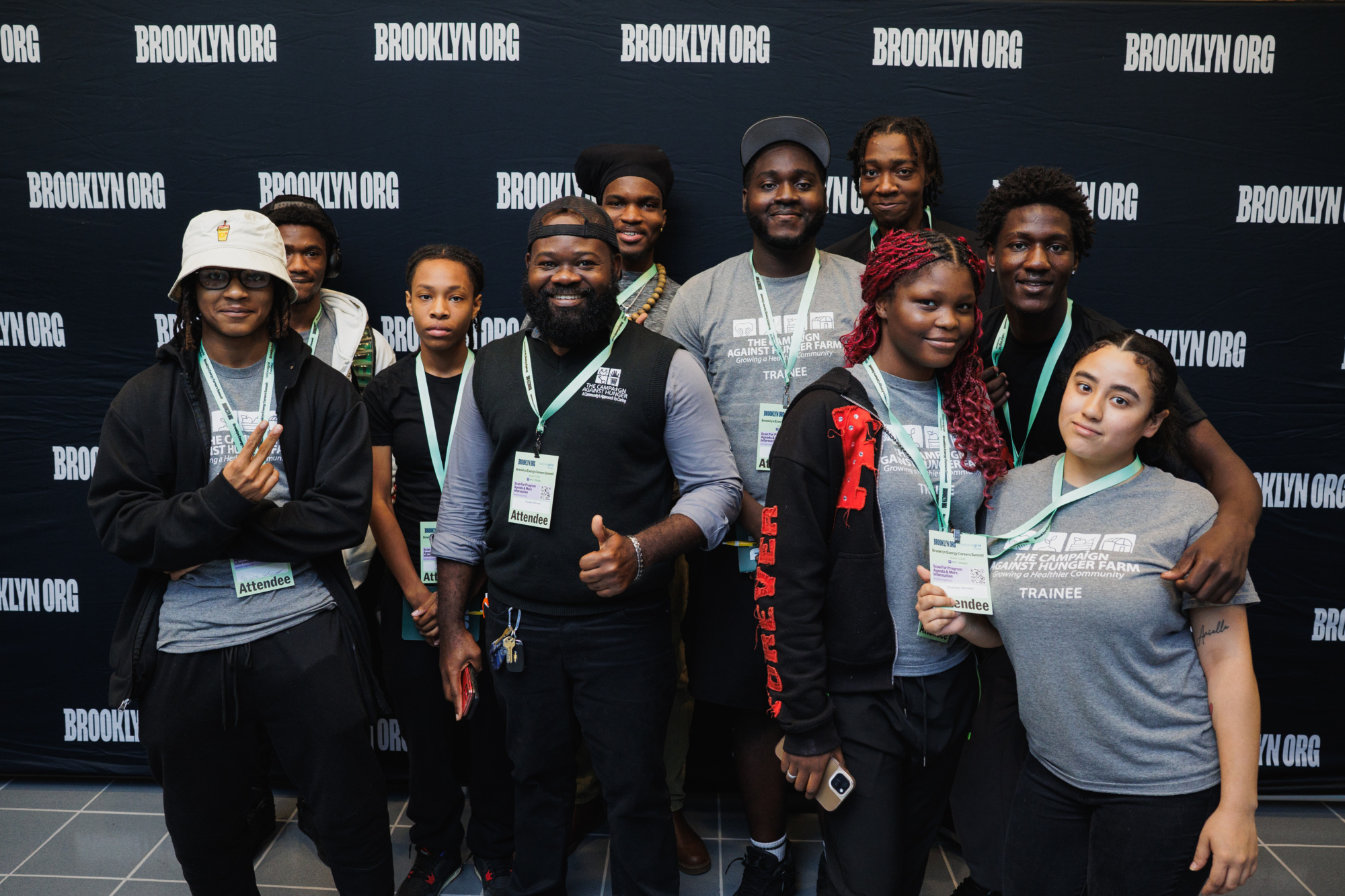 A group of people wearing “Brooklyn Org” event lanyards pose in front of a branded black backdrop.