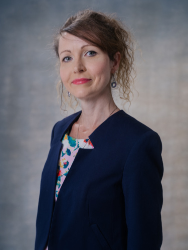 Portrait of a woman wearing a navy blue blazer over a floral patterned top.
