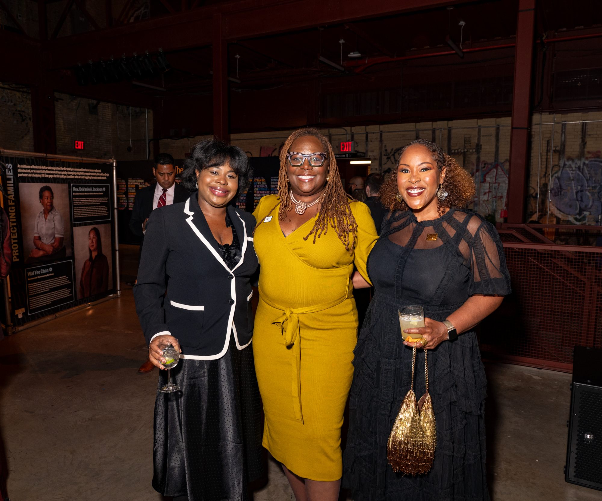 Three women posing for a photo at an event, with two holding drinks.